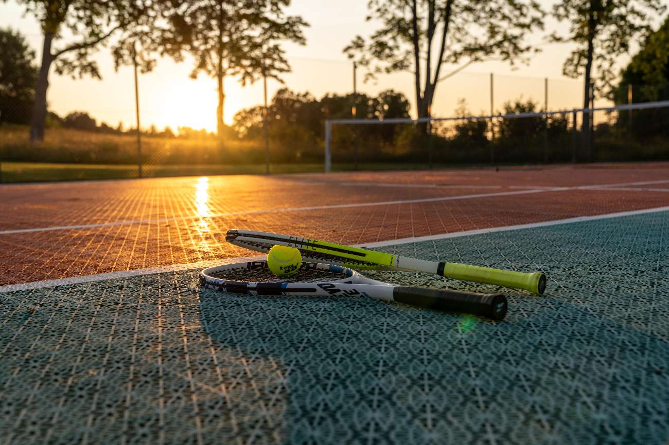 Tennisracket och boll på banan i solnedgången